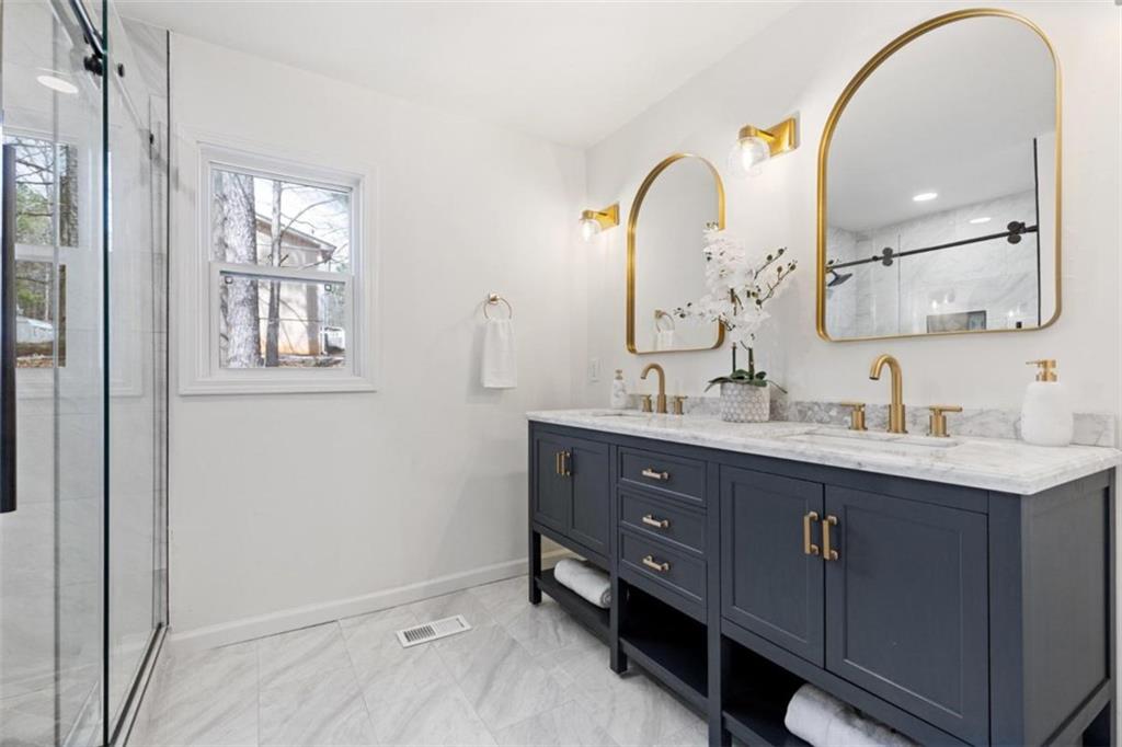 Styled primary bathroom with navy vanity, marble counter and brass mirrors
