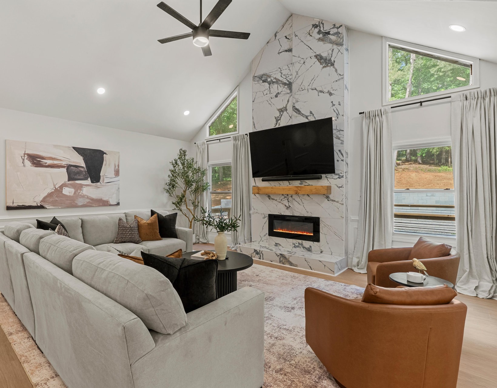 Light filled living room with vaulted ceiling, marble fireplace wall, gray sectional sofa and cognac leather chairs